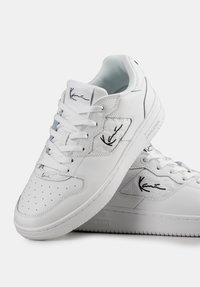 Adidași albi din piele texturată cu vârf perforat, design cu șireturi și detaliu cu logo-ul negru pe lateral și pe limba pantofului.