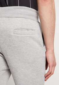 Grijze joggingsbroek met een ribgebreide tailleband, gladde textuur, zijzakken en minimalistisch ontwerp, getoond vanuit de achterkant.