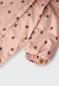 Roze gewatteerde stof met een lieveheersbeestjespatroon, voorzien van elastische manchetten en een bruine leren label. Gladde textuur, lichtgewicht ontwerp.