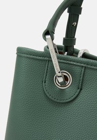Zelená kožená kabelka s texturou hrubého povrchu, stříbrným kováním a smyčkovou rukojetí s nastavitelným popruhem.