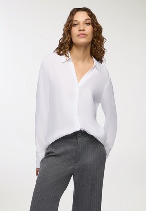Blusa bianca a maniche lunghe con apertura a bottoni e vestibilità rilassata, abbinata a pantaloni grigi a righe sottili con bottone in vita.