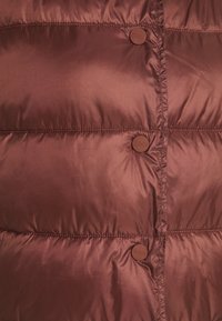 Bruine pufferjack sectie met horizontale gestikte naden, matte afwerking en ronde drukknoopsluitingen met gegraveerde branding. Gladde stoftextuur.