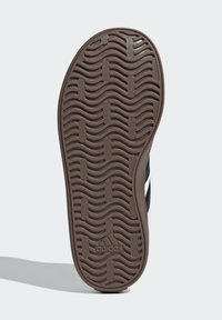Podeszwa brązowego buta Adidas z falistym wzorem bieżnika i prostokątnymi blokami chwytającymi, z widoczną częścią czarno-białej cholewki.