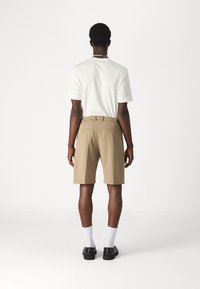 Khakishorts mit Gesäßtaschen, einem knitterfreien Design und einer taillierten Passform, kombiniert mit einem weißen T-Shirt und schwarzen Schuhen. Weiße Socken sind sichtbar.