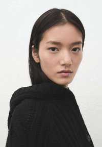 Suéter negro de punto con capucha, presenta un patrón texturizado y botones. La modelo tiene cabello lacio y oscuro, con un fondo neutro.