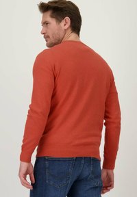 Roestkleurige trui met lange mouwen en een ronde halslijn, met ribgebreide manchetten en zoom. Draagt u met donkerblauwe jeans, die een gestructureerde breistofafwerking tonen.