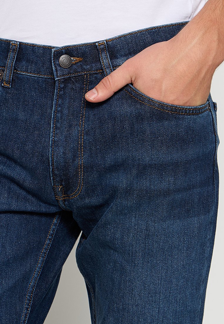 Granatowe dżinsy z klasycznym pięciokomorowym krojem, wykonane z denimu z kontrastującymi pomarańczowymi przeszyciami i metalowym zapięciem.
