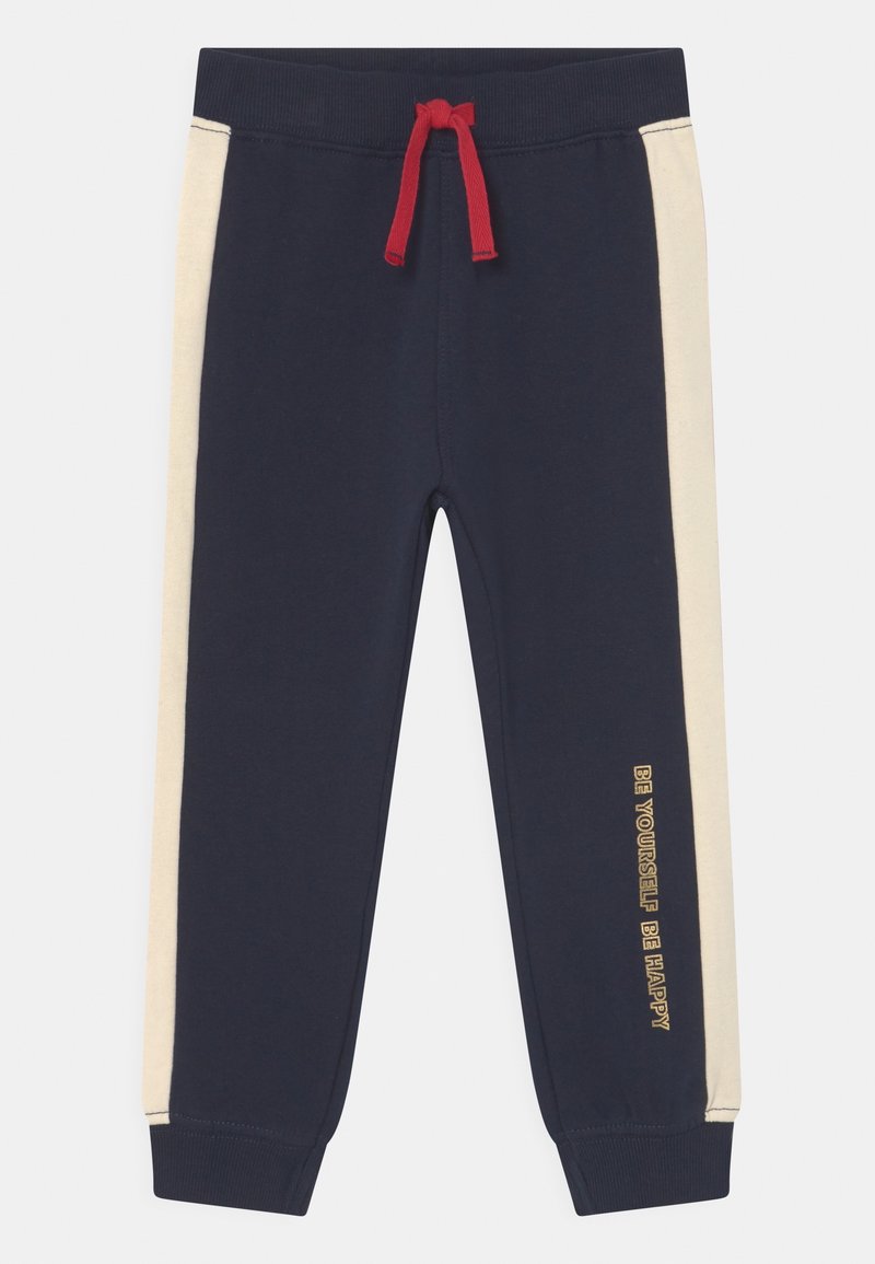 Pantalon de survêtement bleu marine pour enfants avec rayures latérales crème, cordon rouge, poignets côtelés et inscription "Sois toi-même, sois heureux" sur la jambe droite.