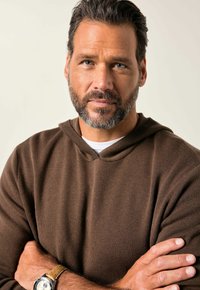 Felpa marrone a maglia con finitura testurizzata, caratterizzata da un collo a V e maniche lunghe. Gli accessori includono un orologio con cinturino in pelle color cammello.