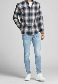 Karierter Flanellhemd in Navy, Weiß und Rot, kombiniert mit hellblauen Skinny Jeans und weißen Sneakers. Hemd mit Knopfleiste und hochgekrempelten Ärmeln.