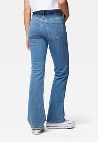 Jeans de mezclilla ajustados de corte acampanado en azul, con cinco bolsillos, lavado claro y detalles de costura sutiles. Combinados con zapatillas blancas.