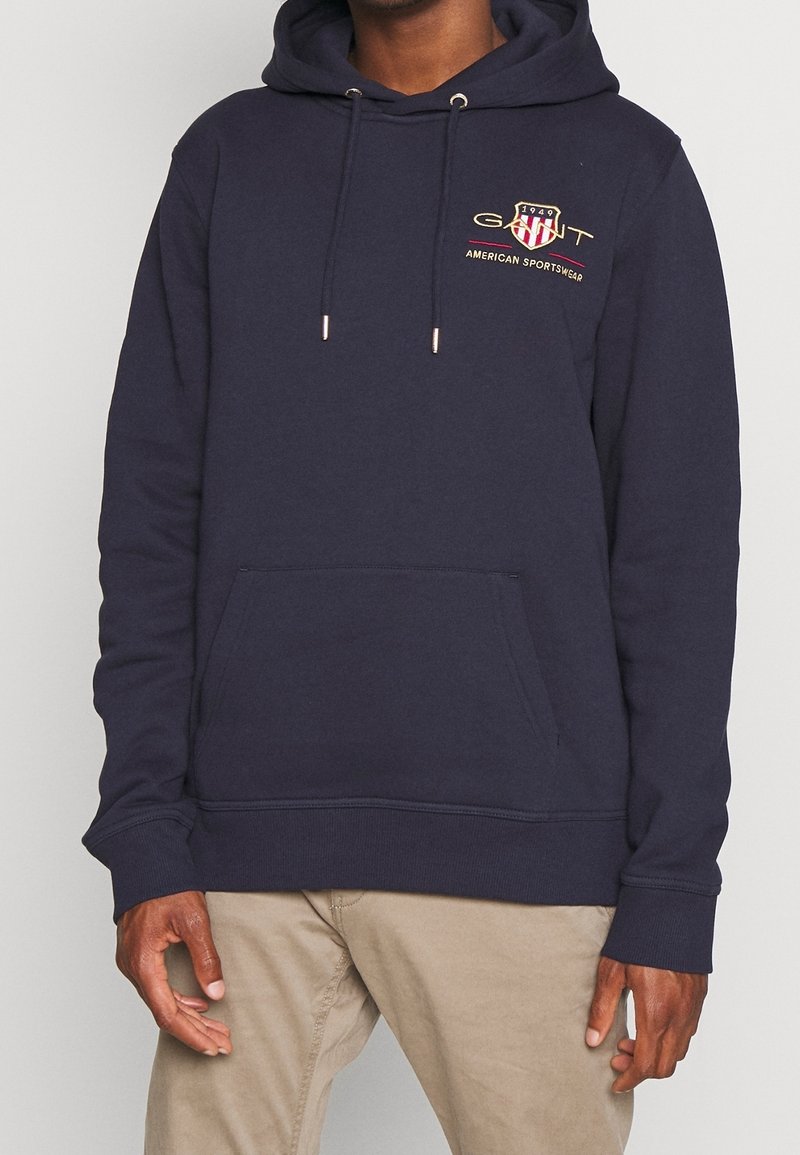 Sudadera azul marino de mezcla de algodón, con un bolsillo canguro en la parte frontal, cordones ajustables y un logo bordado en el pecho.