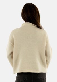 Suéter de punto color crema con cuello alto falso, hombros caídos y corte relajado. Textura suave y longitud corta a la altura de la cintura.