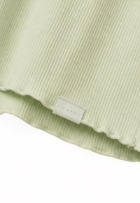 Tissu côtelé vert clair avec une petite étiquette blanche rectangulaire cousue près de l'ourlet inférieur indiquant "OH APRIL."