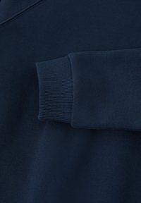 Tumma laivansinisestä collegepaidasta, jossa on sileä pinta. Varressa ribbireunus ja hieman teksturoitu vartalo. Yksinkertainen, minimalistinen muotoilu.