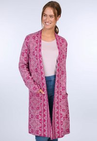Pink patterned long cardigan with floral design, featuring open front, pockets, and relaxed fit. Worn over a light pink top and blue jeans.