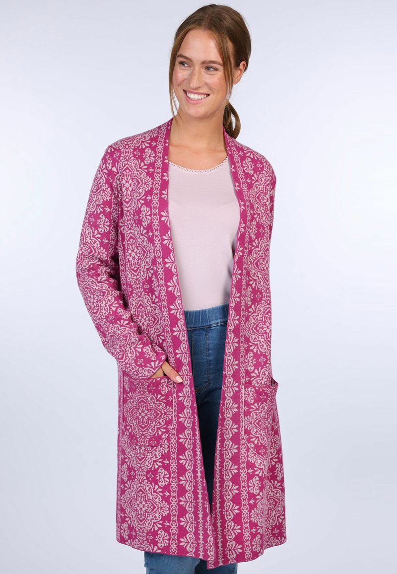 Pink patterned long cardigan with floral design, featuring open front, pockets, and relaxed fit. Worn over a light pink top and blue jeans.