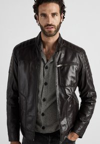 Herrers svart läderjacka med texturerade axelpartier, fickor med dragkedja och slim fit. Bärs över en svart och vit randig skjorta.