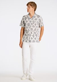 Camisa de botones de manga corta en crema con un patrón floral negro; combinada con pantalones blancos y zapatillas ligeras. Cuello sencillo y ajuste relajado.