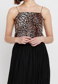 Leopard print satin top with thin spaghetti straps, paired with a pleated black skirt. Features a smooth texture and structured design.