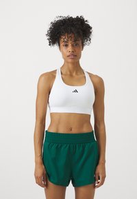 Soutien-gorge de sport blanc avec un logo noir, associé à un short vert avec une taille élastique et une coupe ample.