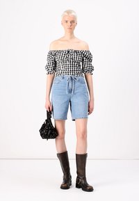 Off-the-shoulder black and white gingham top, light blue denim shorts, black floral handbag, and knee-high brown leather boots.