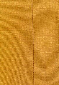 Gultyg med en texturerad väv, som har en rak söm som går vertikalt med en lätt glans.