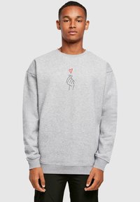 Gray sweatshirt featuring a simple black line drawing of a hand making a heart gesture, with a small red heart above it.