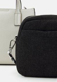 Sac bandoulière en tissu noir avec fermoir argenté devant un sac cabas en cuir blanc texturé avec poignées verticales.