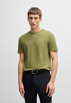 Olive green textured t-shirt with a round neckline, short sleeves, paired with black trousers and a black belt featuring a silver buckle.