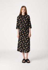 Mustaga lillemustriga kleit, millel on kolmveerandi varrukad, nööbid eest ja vöö. Sellel on kollased ja valged lillemustrid. Mudel kannab musti sandaale.