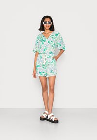 Conjunto de duas peças com padrão floral, apresentando uma blusa de manga curta e decote em V, e calções combinando. Feito de tecido leve, com cintura ajustável e bordas em forma de ondas.