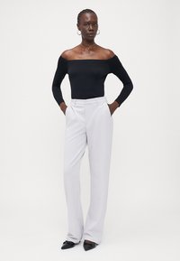 Sort off-the-shoulder bodysuit i svart, kombinert med høy midje lys grå bukser. Modellen accessorizerte med hoop øredobber og en gullkjede.
