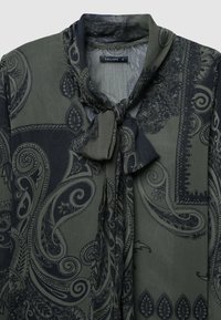 Dunkelgrünes Hemd mit Paisleymuster in Marineblau, mit gebundenem Ausschnitt und leichtem, strukturiertem Stoff. Das Markenlabel lautet "CALLIOPE."
