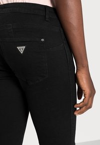 Sorte denimjeans med høy midje, med en trekantet logopatch på baklommen og en tettsittende silhuett. Glatt tekstur.