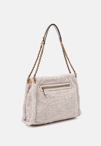 Borsa in pelliccia sintetica beige con manici a catena dorati, chiusura con zip superiore e tasca con zip frontale. Presenta bordi arrotondati e una consistenza morbida.