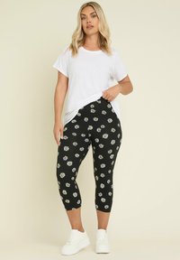 Svarta leggings med vitt och gult prästkrage-mönster, kort längd, ihop med en löst sittande vit t-shirt och vita sneakers.