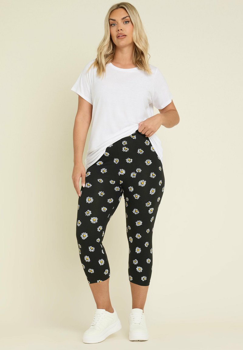 Svarta leggings med vitt och gult prästkrage-mönster, kort längd, ihop med en löst sittande vit t-shirt och vita sneakers.