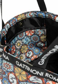 Bolsa de tela texturizada con un interior colorido y geométrico que presenta motivos circulares y estelares. Incluye una correa negra y cierre a presión.