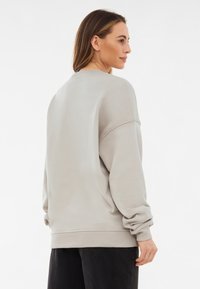 Sudadera de gran tamaño en gris claro, con puños y dobladillo acanalados, que presenta un diseño sencillo y una textura suave. La parte posterior es lisa y tiene un ajuste relajado.
