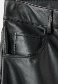 Primo piano di pantaloni in pelle nera che mostrano una tasca anteriore, un passante per cintura e cuciture dettagliate.