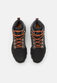 Czarne, zamszowe buty turystyczne z pomarańczowymi sznurowadłami, szarymi akcentami i gumowymi podeszwami. Posiadają metalowe oczka i wyściełany kostek dla komfortu.