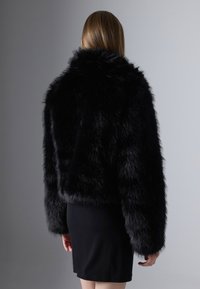 Zwarte faux fur cropped jas met een hoge kraag en lange mouwen, met een pluche textuur en een getailleerde silhoutte, gecombineerd met een zwarte rok.