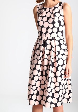 Robe noire sans manches avec de grands pois roses, dotée d'une jupe plissée et d'un détail nœud au niveau de l'encolure. Texture de tissu lisse.