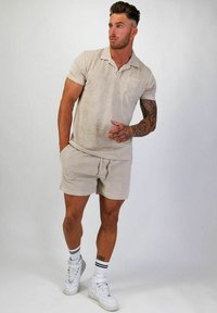 Beige pikétröja och matchande shorts i texturerad tyg, med en bröstficka. Buren med vita högklackade sneakers och randiga strumpor.