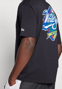 Svart bomullströja med en färgglad "World Series 1998" grafik på baksidan. Korta ärmar, rund hals och enkel design.