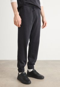 Black cotton joggers with an elastic waistband, drawstring closure, and elastic cuffs. Paired with black sneakers and white socks.