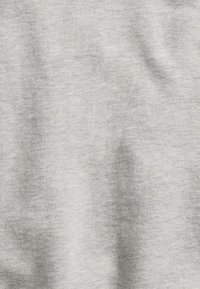 Gros plan sur une texture de tissu gris clair avec des plis doux et un ombrage subtil.