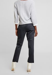 Szary sweter z rękawami o długości trzy czwarte, w połączeniu z czarnymi spodniami w kratę i białymi botkami na obcasie sięgającymi kostki. Prosty design, minimalna ilość detali.