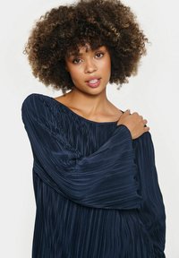 Námornícky pletený dlhý rukáv blúzka so širokým výstrihom a textúrovanou tkaninou, s jemným drapovaním a voľným strihom okolo ramien.